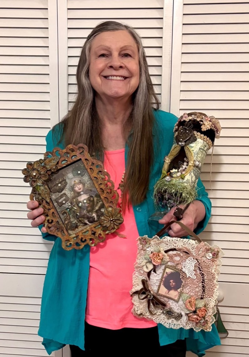 Barbara DeLisle holding several of her mixed-media assemblage pieces.