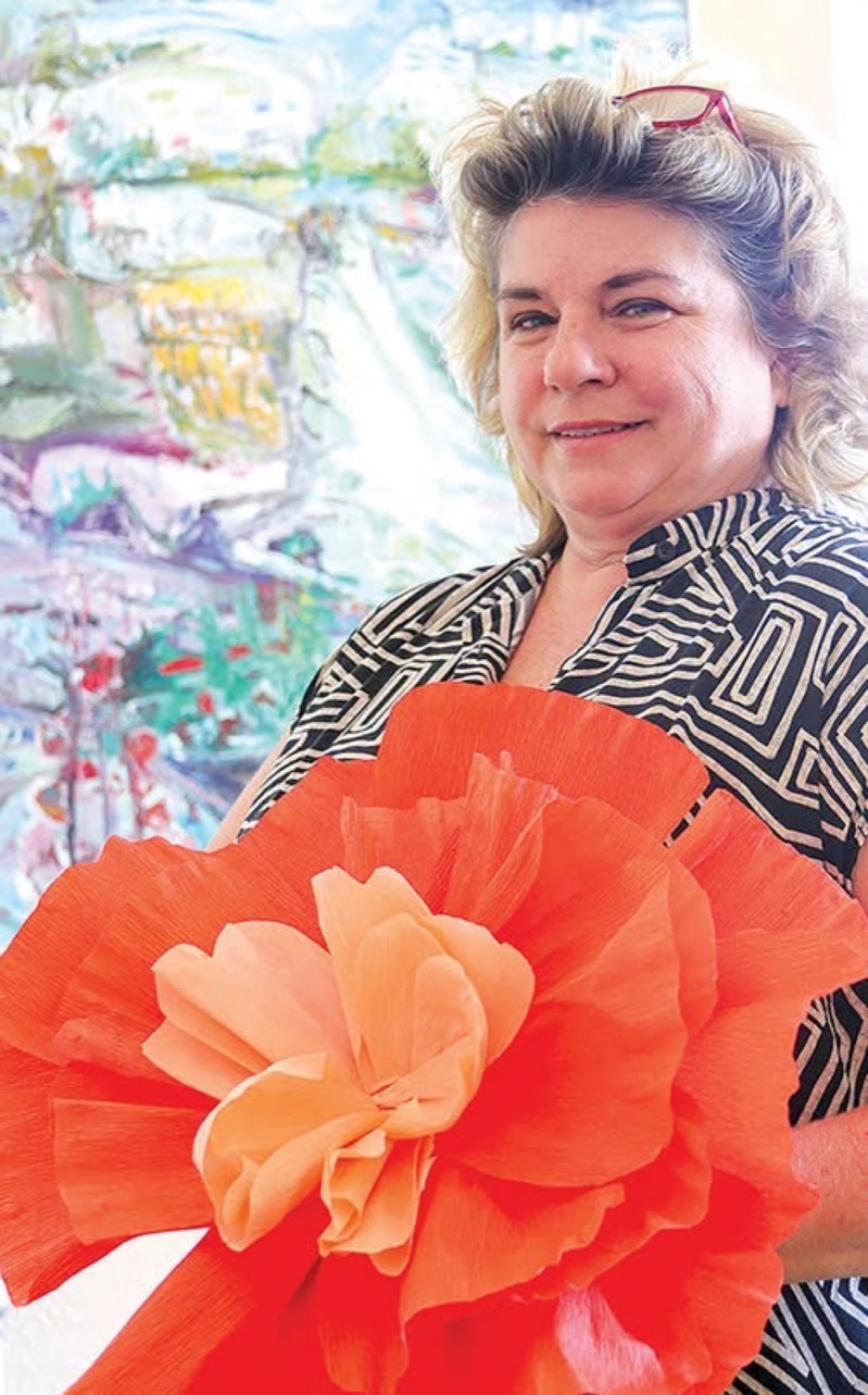Shelley Schenker with one of her paintings and a giant paper flower.
